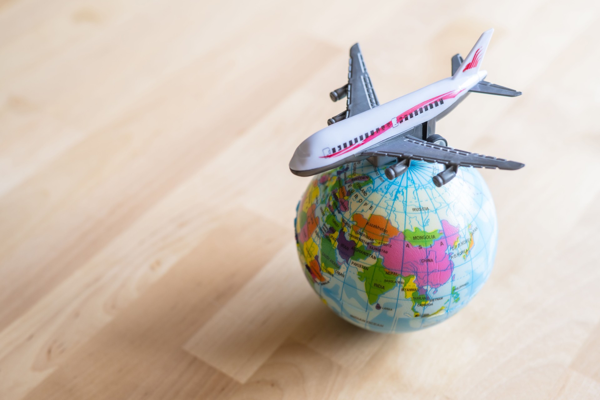 Miniature airplane soaring above a small globe, zooming in on asia, resting on a wooden table, symbolizing the excitement of world tours and global adventures in travel